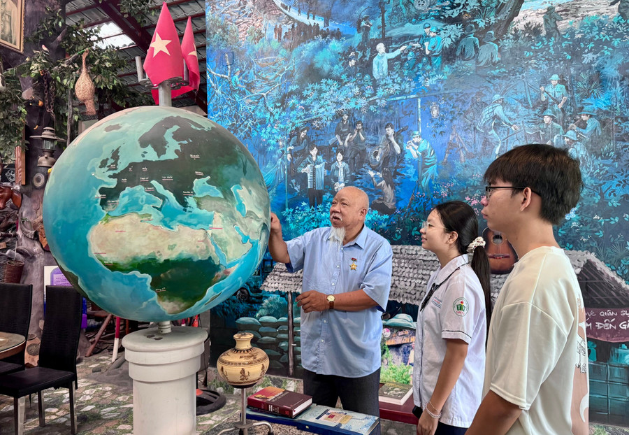Cựu chiến binh Lâm Xuân Quang cùng học sinh tham quan quả địa cầu, tái hiện hành trình ra đi tìm đường cứu nước của Bác Hồ. Ảnh: Thùy Linh