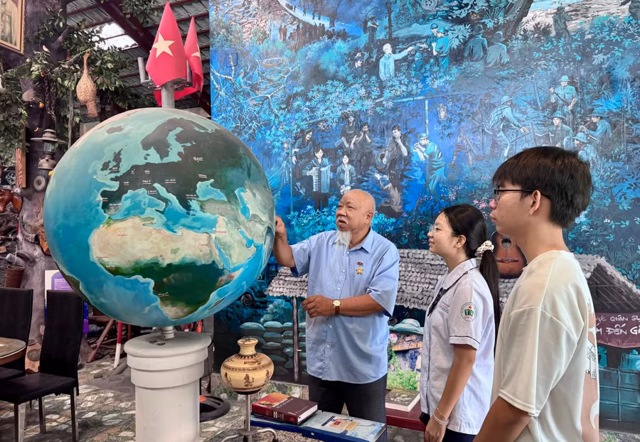 Cựu chiến binh Lâm Xuân Quang cùng học sinh tham quan quả địa cầu, tái hiện hành trình ra đi tìm đường cứu nước của Bác Hồ. Ảnh: Thùy Linh