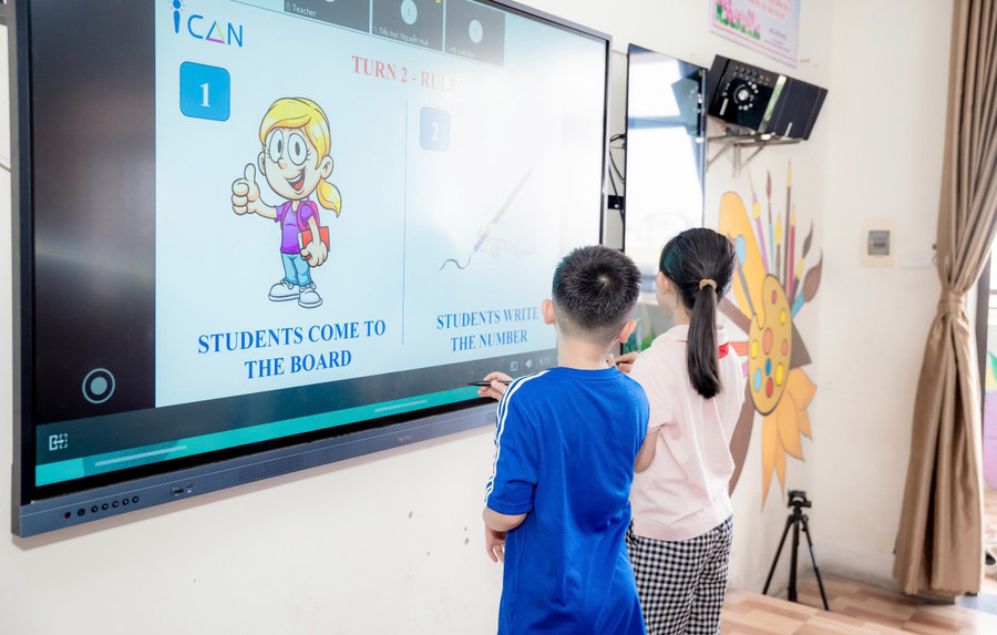 Học sinh thực hành bài tập trên bảng tương tác với phần mềm chuyên dụng để giáo viên chữa bài tức thời. dua-giao-vien-ban-ngu-va-giao-trinh-chuan-quoc-te-toi-tung-lop-hoc-2.jpg