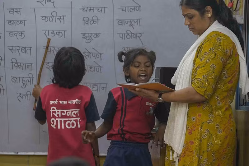 Cô giáo Sunita Patil kiểm tra vở của Vaishali Pawar, 10 tuổi, ở giữa, tại trường Signal Shala. Ảnh: AP. chum-anh-ngoi-truong-duoi-duong-cao-toc-o-an-do-023.jpg
