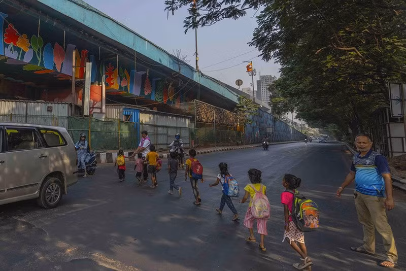 Khoảng một chục trẻ em đang tạo thành những mảng màu nhỏ trên đường nhựa xám xịt khi chúng băng qua một con đường đông đúc được 2 người giúp đỡ. chum-anh-ngoi-truong-duoi-duong-cao-toc-o-an-do-02.jpg
