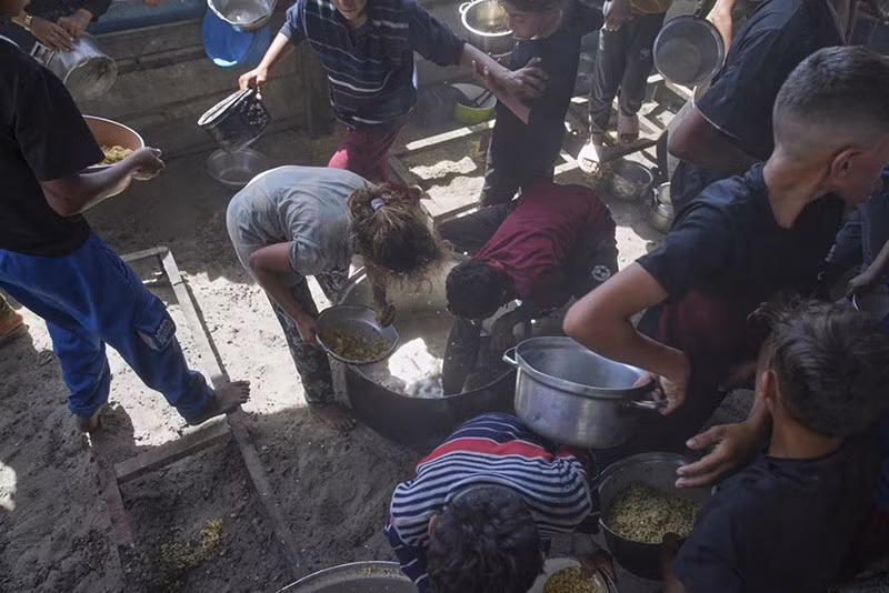 Trẻ em Palestine đang cào một chiếc nồi để tìm thức ăn thừa. (Ảnh AP/Abdel Kareem Hana) chum-anh-lhq-canh-bao-ke-hoach-phan-phoi-vien-tro-gaza-0505-03.jpg