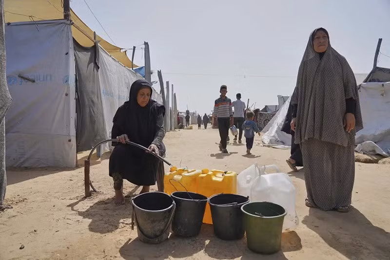 Những người Palestine đang đổ nước vào can nhựa từ một đường ống tại một trại lều ở Khan Younis, Dải Gaza. (Ảnh AP/Abdel Kareem Hana) chum-anh-lhq-canh-bao-ke-hoach-phan-phoi-vien-tro-gaza-0505-011.jpg