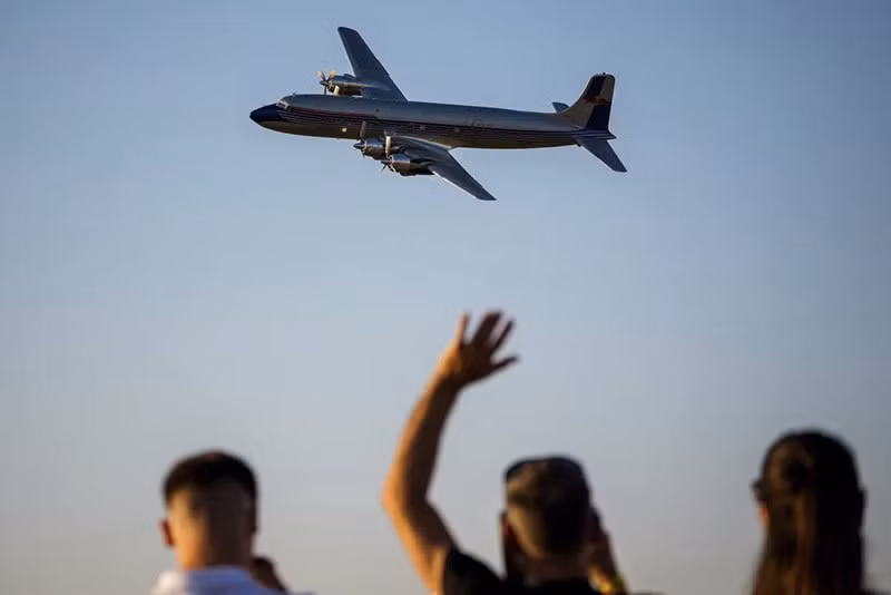 Mọi người vẫy tay khi chiếc máy bay Douglas DC-6B của đội nhào lộn Flying Bulls Red Bull bay qua đường băng tại sân bay Aurel Vlaicu trong ngày đầu tiên của triển lãm. chum-anh-trien-lam-hang-khong-quoc-te-bucharest-2025-02.jpg