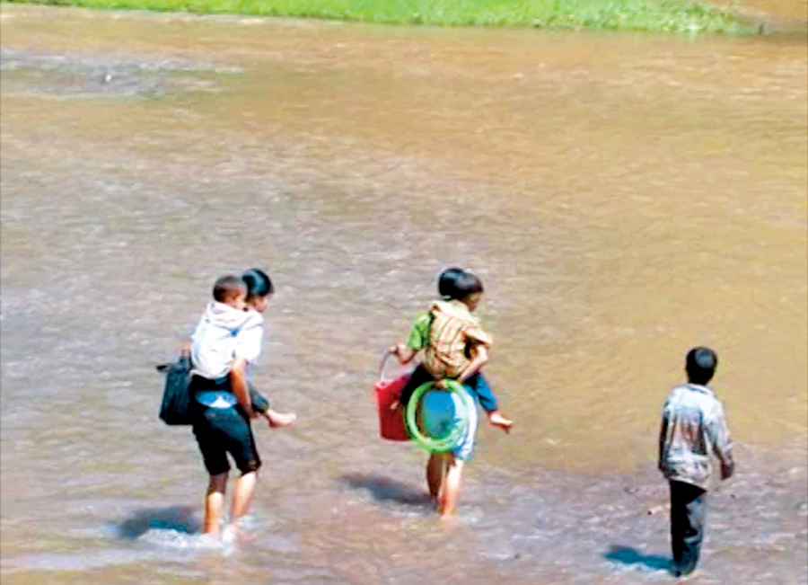 Cô giáo hỗ trợ HS đưa em qua suối trên đường trở về nhà sau buổi học