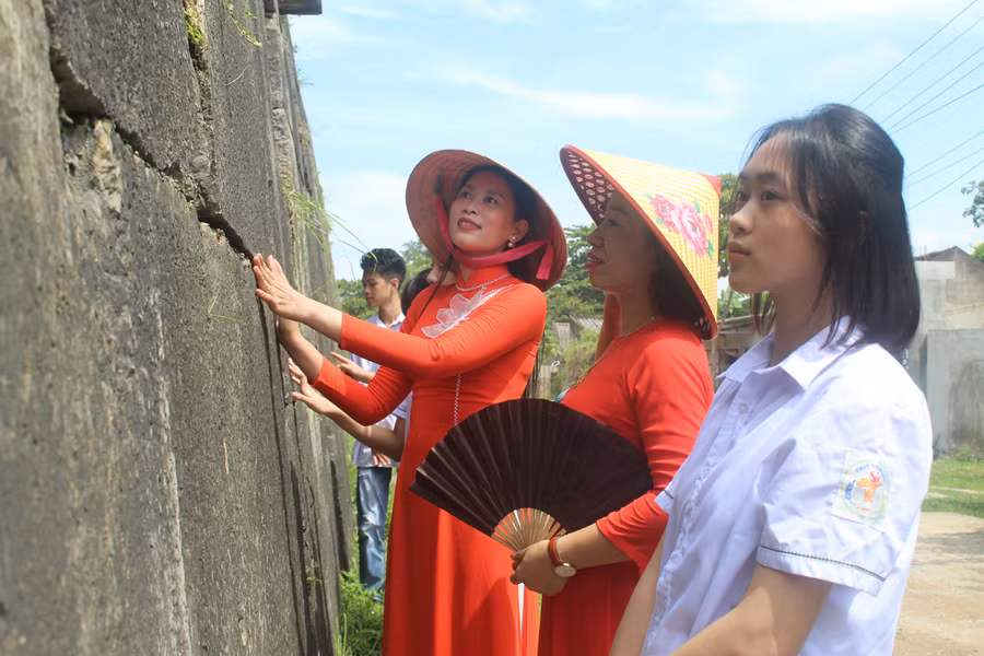 Cô Quách Lan Anh (áo đỏ từ phải qua) cùng học sinh nghe hướng dẫn viên giới thiệu về kiến trúc tường Thành nhà Hồ. Ảnh: LT.