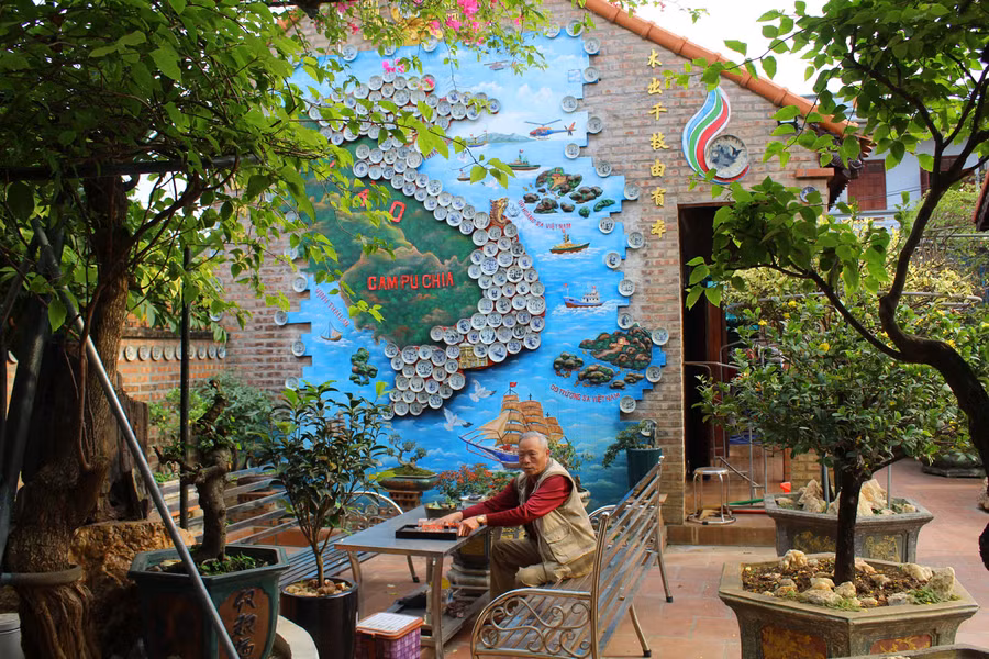 Ông Lê Xuân Năm bên bức tranh bản đồ Việt Nam được ghép từ hàng trăm chiếc đĩa. Ảnh: LT.