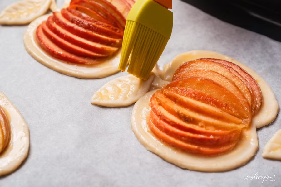 Đánh đều 1 lòng đỏ trứng gà với 2 thìa to sữa tươi, rồi dùng chổi phết lên phần rìa bột, không phết lên phần táo.