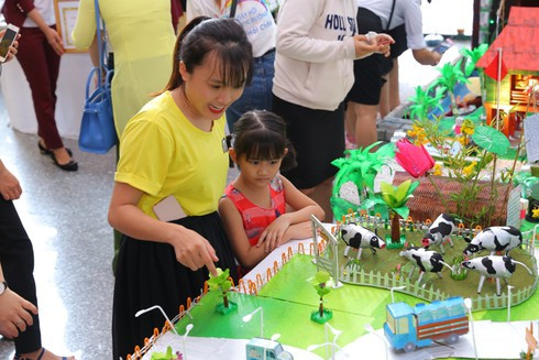 Cô giáo và các em học sinh bên cạnh những mô hình làm từ vỏ hộp sữa trong chương trình SHĐ