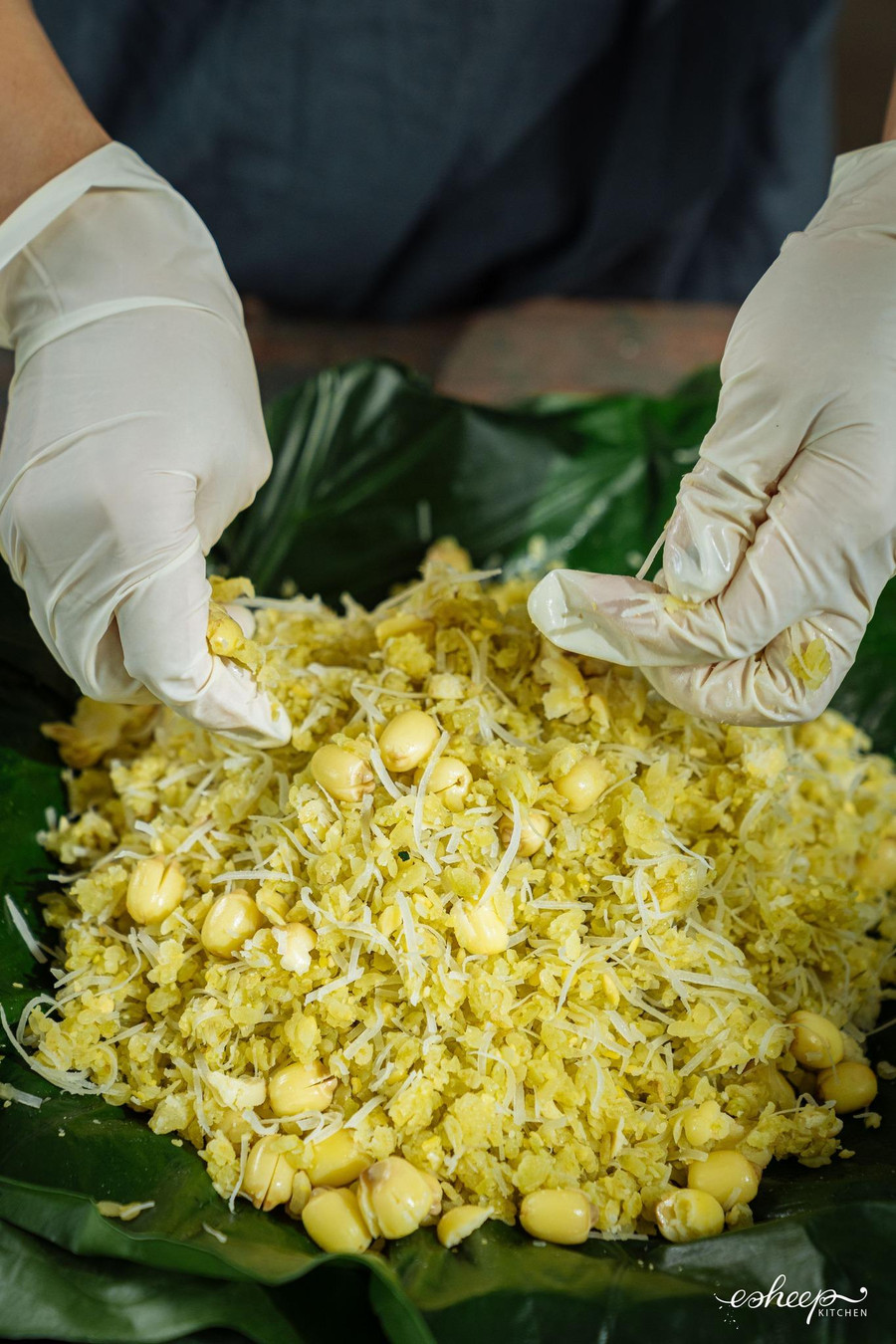 Tiếp tục trộn cùng dừa sên và hạt sen thật đều và nhanh tay để xôi cốm không nát. Để xôi cốm mềm và thơm hơn, bạn ủ bằng lá ráy và thêm một lớp lá sen mỏng.