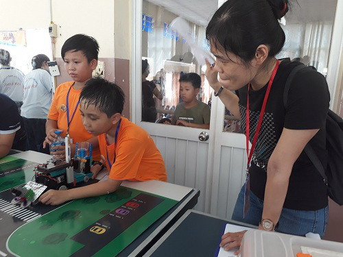 Một học sinh điều khiển robot và mồ hôi thấm ướt cả mái đầu em. Bên cạnh, một nữ thành viên Ban tổ chức vừa chăm chú theo dõi vừa dùng mảnh giấy làm mát cho cậu bé. Một học sinh điều khiển robot và mồ hôi thấm ướt cả mái đầu em. Bên cạnh, một nữ thành viên Ban tổ chức vừa chăm chú theo dõi vừa dùng mảnh giấy làm mát cho cậu bé.