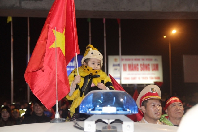 Một em bé được bế lên ngồi trên cao để chờ đón cầu thủ