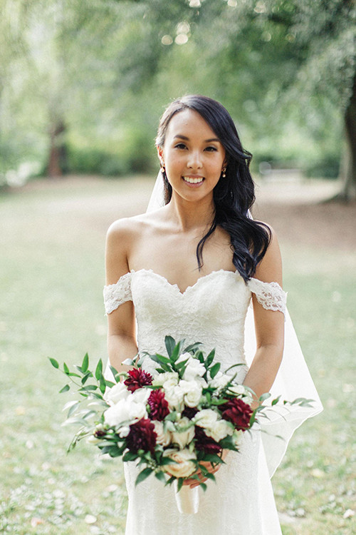 Cô dâu xuất hiện trong bộ váy trắng trễ vai và cầm trên tay một bó hoa cưới đơn giản với sắc đỏ và trắng.