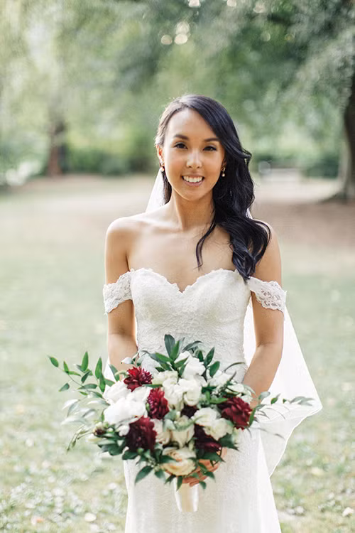 Cô dâu xuất hiện trong bộ váy trắng trễ vai và cầm trên tay một bó hoa cưới đơn giản với sắc đỏ và trắng.