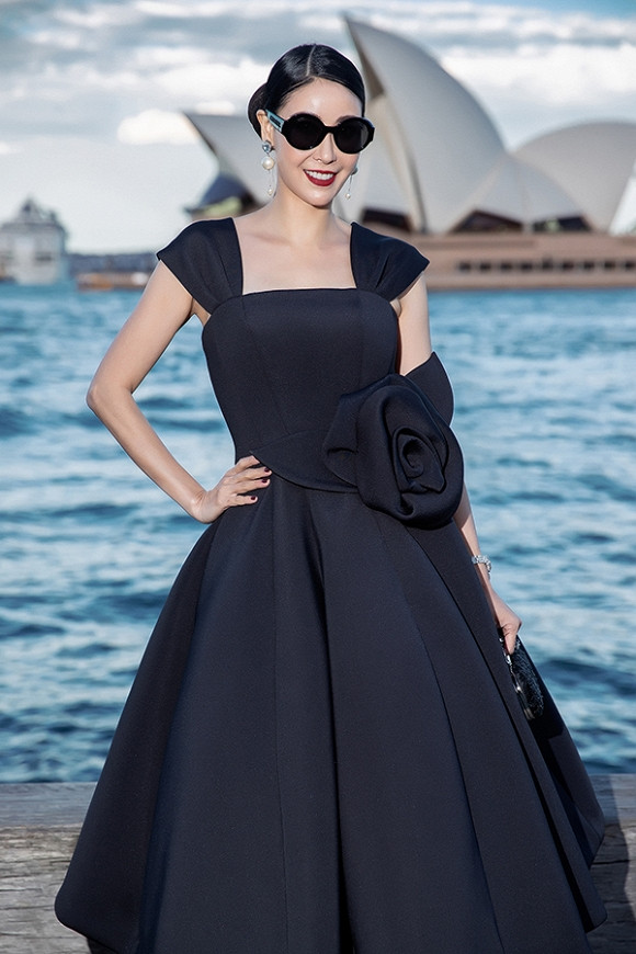 Hoa hậu Việt Nam 1992 Hà Kiều Anh điệu đà, trẻ trung trong dáng váy xoè rộng được tạo nên từ những đường cắt nối tinh tế. Thắt eo được nhấn nhá với hoạ tiết hoa 3D. Hà Kiều Anh phối bộ cánh cùng áo clutch, mắt kính to bản, hoa tai ngọc trai.