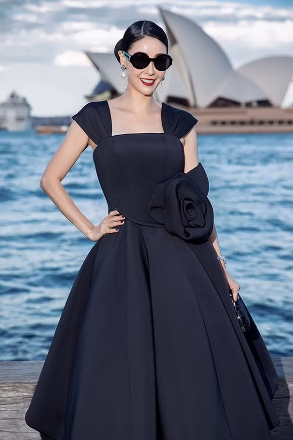 Hoa hậu Việt Nam 1992 Hà Kiều Anh điệu đà, trẻ trung trong dáng váy xoè rộng được tạo nên từ những đường cắt nối tinh tế. Thắt eo được nhấn nhá với hoạ tiết hoa 3D. Hà Kiều Anh phối bộ cánh cùng áo clutch, mắt kính to bản, hoa tai ngọc trai.