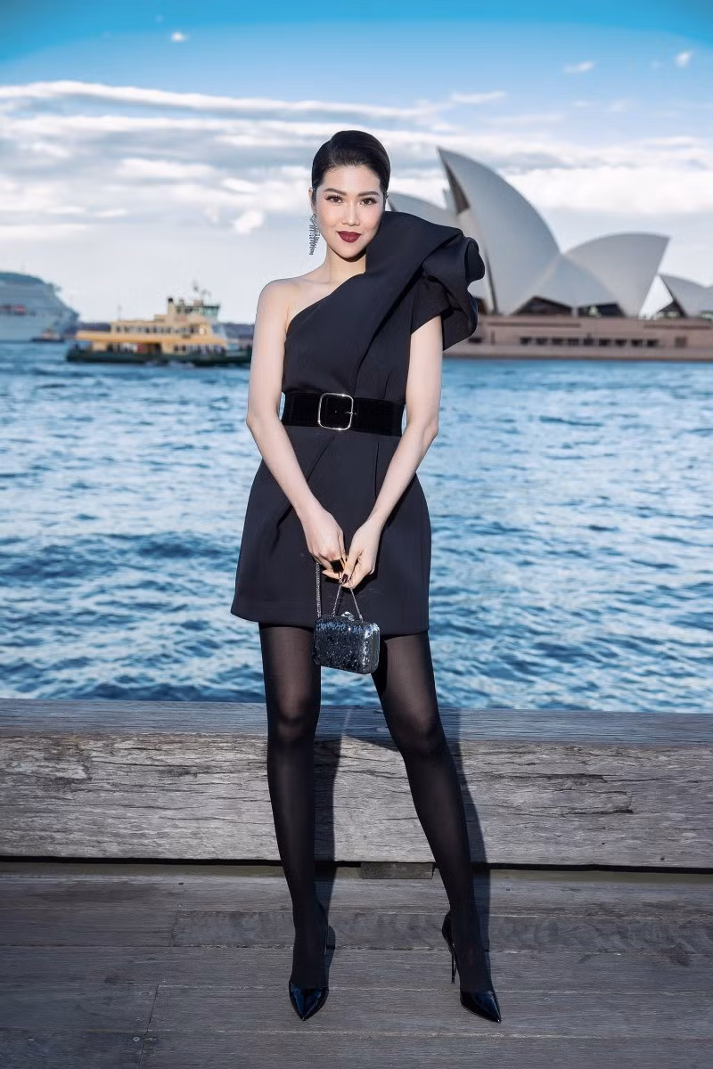 Siêu mẫu Thu Hằng khoe chân dài trong thiết kế đầm cocktail lệch vai, tạo phom 3D to bản ở cầu vai. Người đẹp phối trang phục cùng thắt lưng to, clutch, giày cao gót mang cùng tất đen dài, hoa tai ánh bạc to bản.