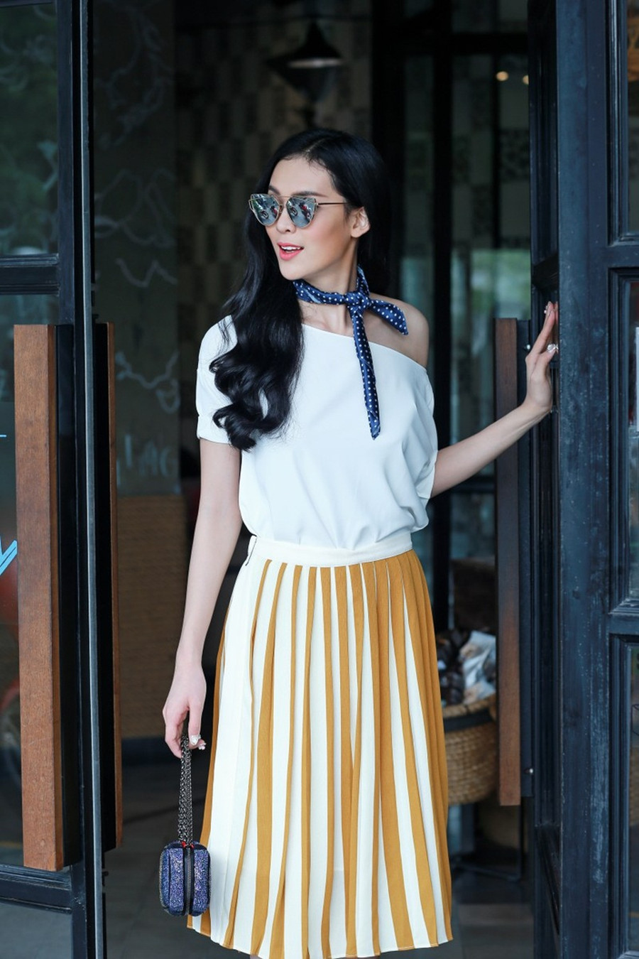 Trong ảnh dáng váy xếp ly xòe được may trên nền vải màu vàng tươi mix với áo lệch vai giúp người mẫu khoe làn da trắng rạng rỡ.