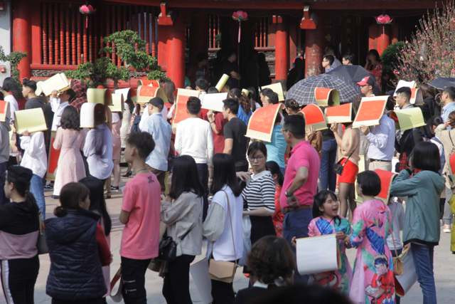 Sáng mồng 2 Tết thời tiết tại Hà Nội khá nóng, nhiều người xếp hàng đã lấy những tờ xin chữ của mình để tránh nắng