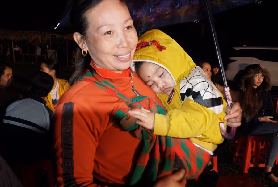 Dù đã về khuya nhưng người mẹ này vẫn địu con, cầm ô che mưa cho con, tiếp tục dõi theo chương trình