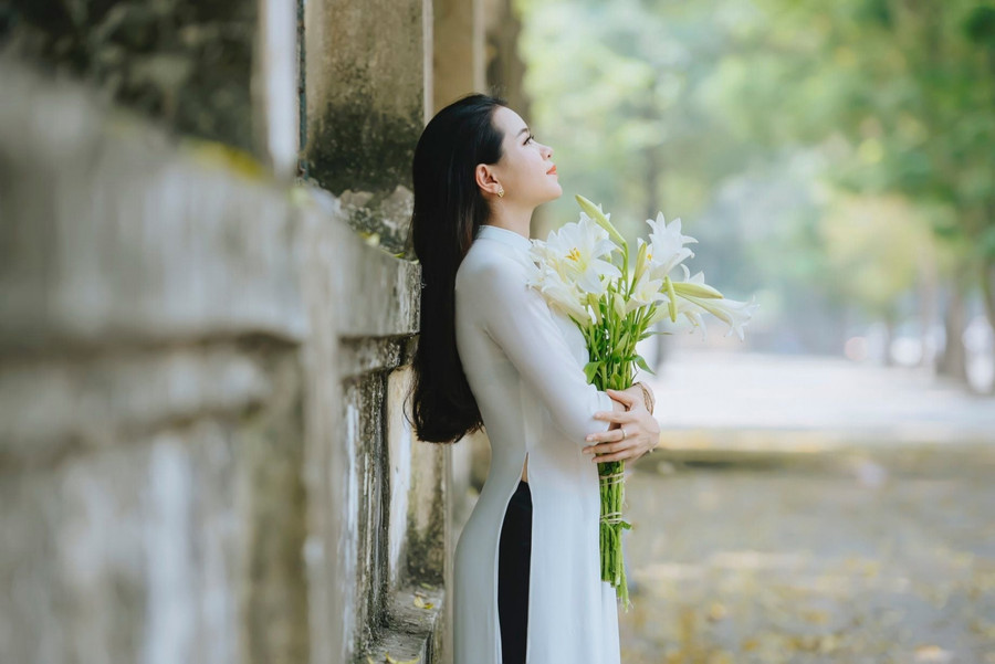 Bạn đứng khép chân lại rồi nhẹ nhàng cầm hoa trên tay có thể đưa gần lên mũi nếu bạn không tự tin về nụ cười của mình hoặc đặt hoa sang 1 bên tay như khi ôm bó hoa cưới dáng dài vậy. Ảnh: Nắng Studio