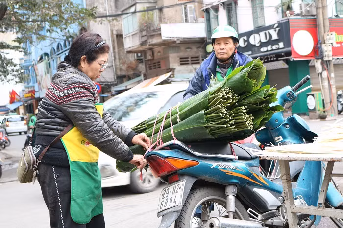 Vội vàng bê chồng lá dong ra cho khách, một tiểu thương chia sẻ: Nhìn chung lá dong trong dịp Tết này bán chạy, chạy hơn cả năm ngoái. Thu nhập của người bán vì thế cũng khá hơn, dù rằng công việc có vất vả.