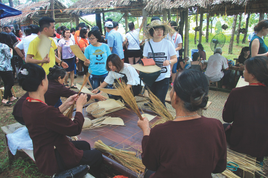 Các bà, các mẹ ở làng cổ Đường Lâm (Sơn Tây, Hà Nội) đang trổ tài bện chổi, đan rổ rá bằng nan bán cho du khách đến tham quan chợ quê