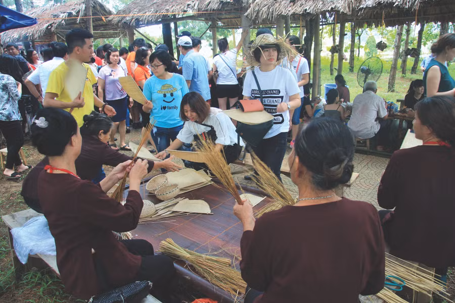 Các bà, các mẹ ở làng cổ Đường Lâm (Sơn Tây, Hà Nội) đang trổ tài bện chổi, đan rổ rá bằng nan bán cho du khách đến tham quan chợ quê
