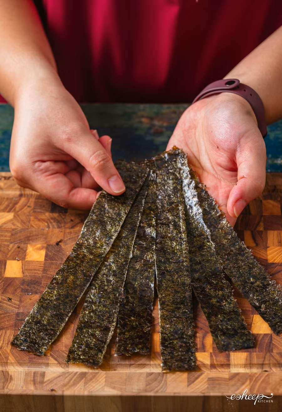 Cắt tấm rong biển cuộn cơm thành các sợi dày chừng 2cm làm “dây nịt” để cố định cuộn cơm.
