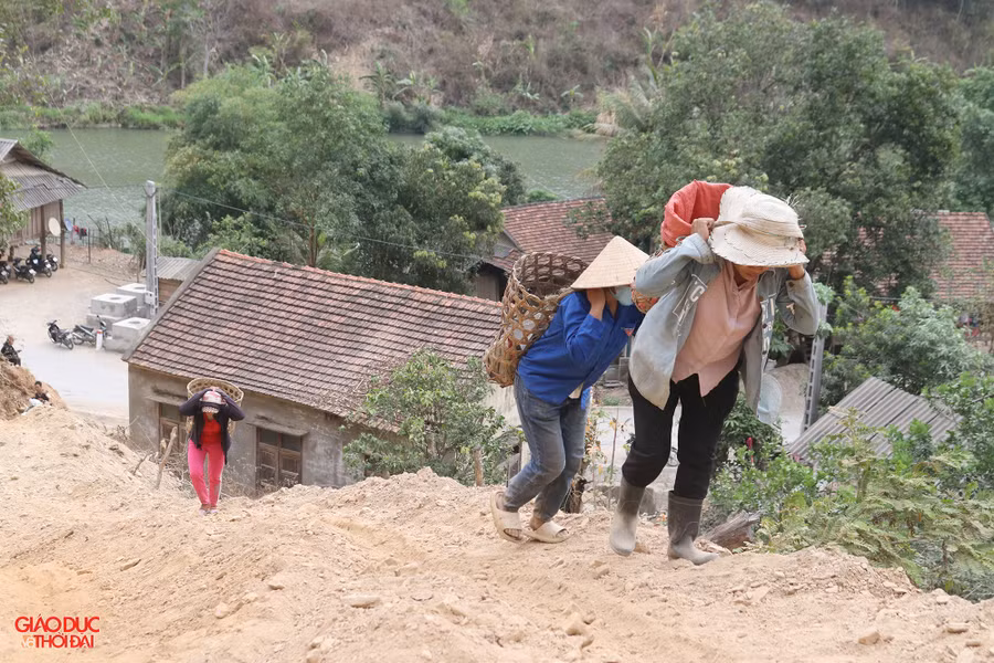 Không đi được xe máy, những người phụ nữ ở bản Nhãn Cù cuốc bộ, leo dốc gùi vật liệu lên bản. Mặc dù đường đi khó khăn, mỗi lần gùi không được nhiều nhưng ai cũng cảm thấy vui vì giúp đỡ được bà con trong bản. Ảnh: Phạm Tâm.