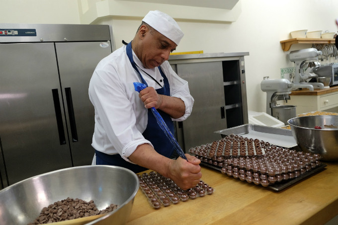 Đầu bếp Stoby nấu chảy chocolate trong một chiếc chậu lớn, sau đó bóp chocolate đầy các khuôn nhỏ có sẵn tạo ra những viên chocolate có hương vị đặc biệt. Về lớp vỏ, đầu bếp cũng sẽ chuẩn bị nhiều lựa chọn khác nhau. Using piping, Chef Stoby fills each chocolate shell with a special chocolate sauce, which has been gently melted in a large mixing bowl. He then seals the truffles before dipping them in the melted chocolate filling to give each one a unique texture, before laying out to set on platters.