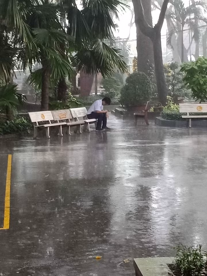 Nam sinh ngồi dầm mưa dưới sân trường.