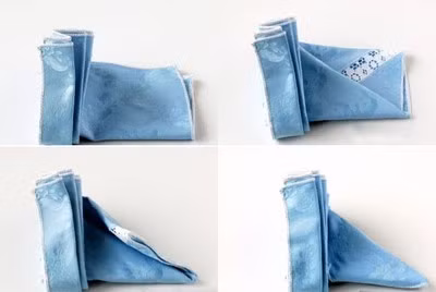 Gấp đôi tấm khăn sau khi đã xếp ly, gấp ½ góc vải trên bên phải vào trong tạo hình tam giác. Sau đó, gấp ½ góc vải dưới bên phải chồng lên trên gài vào trong nếp gấp cánh quạt để làm chân đế tam giác.