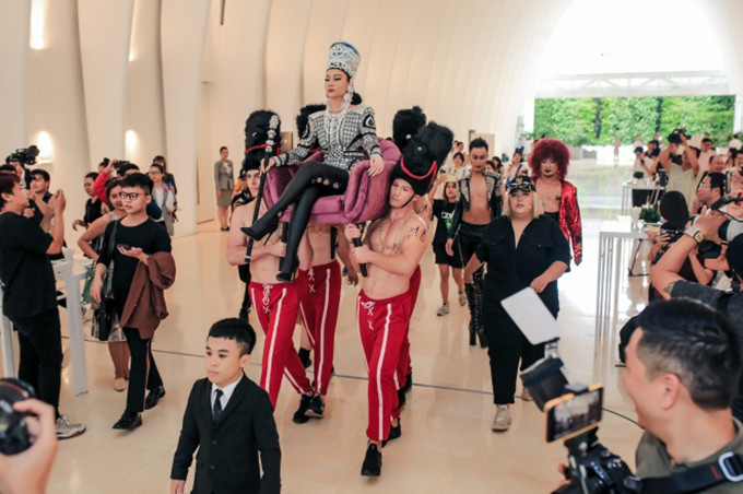 Trong buổi họp báo, nữ ca sĩ “chơi trội” bằng cách xuất hiện ấn tượng bằng cách ngồi trên ghế để dàn mẫu nam khoe hình thể lực lưỡng khiêng.