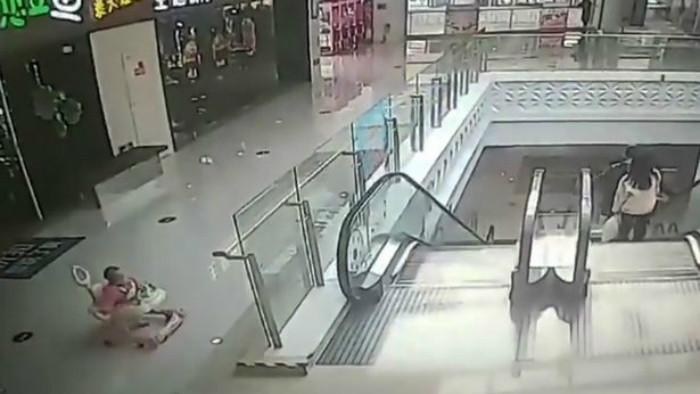 Bé gái sau đó tự di chuyển đến phía thang cuốn và ngã lộn nhào. (Ảnh: AsiaWire) Bé gái 9 tháng tuổi lộn nhào xuống thang cuốn vì cha mẹ lơ là