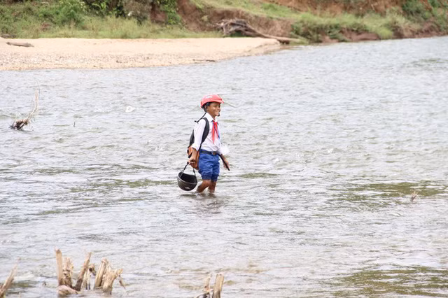 Một nam học sinh lội sông để đến trường