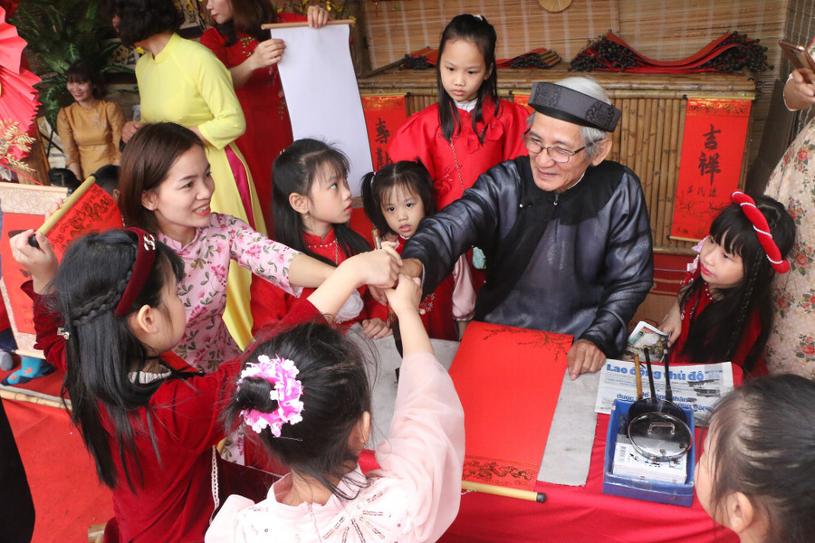 Ông Đồ hướng dẫn các em nhỏ động tác cầm bút mực tàu để viết chữ thư pháp ngày xuân.