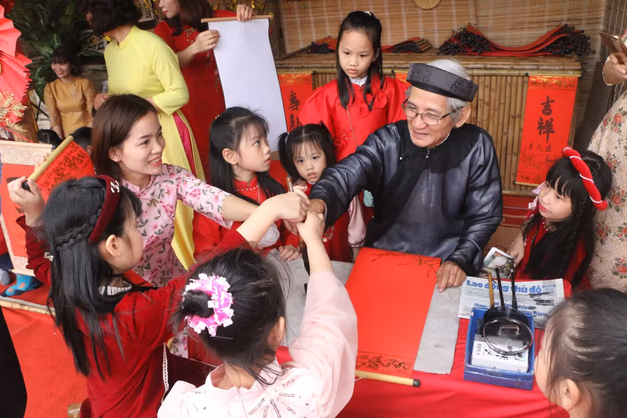 Ông Đồ hướng dẫn các em nhỏ động tác cầm bút mực tàu để viết chữ thư pháp ngày xuân.