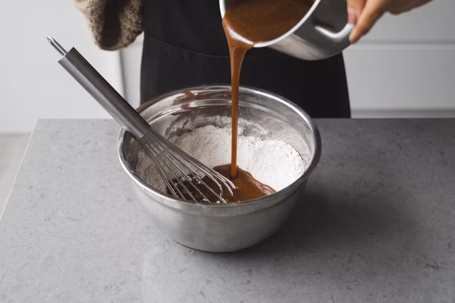 Tạo lỗ nhỏ giữa bột, trút dần hỗn hợp bơ còn ấm vào, nhào, nhồi cho đến khi mịn đều, dẻo.