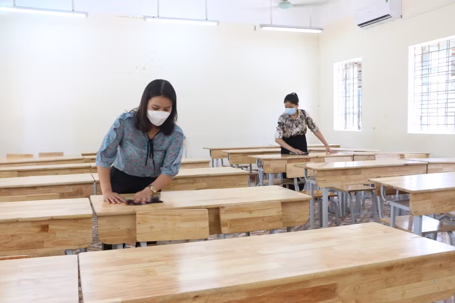 Các giáo viên tiến hành vệ sinh bàn ghế trong phòng thi để sẵn sàng cho buổi thi đầu tiên vào sáng mai, 18/6.