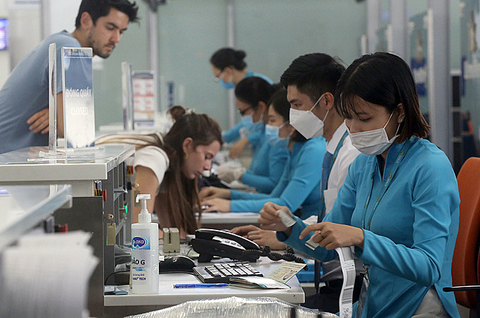 Nhân viênlàm thủ tục check in cho khách tại sân bay Nội Bài thường xuyên tiếp xúc khách nước ngoài không đeo khẩu trang. Ảnh: Bá Đô