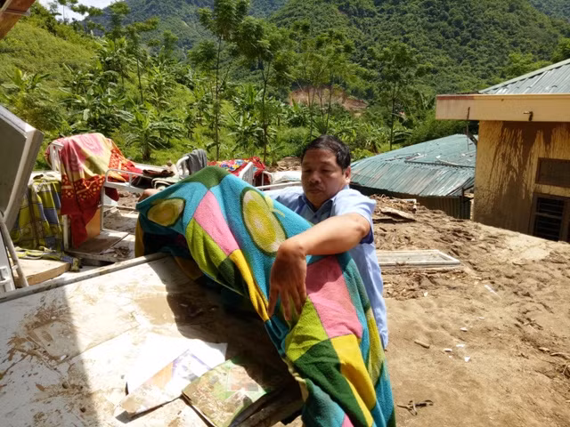 Thầy giáo Phạm Văn Kiên - Hiệu trưởng trường PTDTBT-THCS Tam Chung nhặt nhạnh đồ dùng của học sinh đem ra phơi nắng.