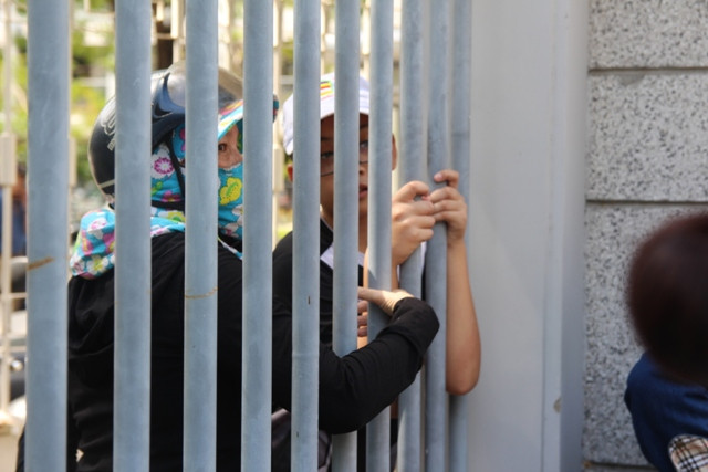 Một phụ huynh đưa mắt ngóng con qua khe cổng sắt.
