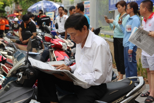 Tấp vội chiếc xe vào lề, một phụ huynh đọc báo trong lúc đợi con.