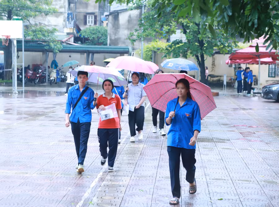 Các thí sinh được lực lượng thanh niên tình nguyện che ô từ cổng vào khu vực để đồ tư trang tại điểm thi Trường THPT Ngô Thì Nhậm, huyện Thanh Trì. 