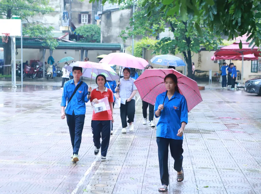 Các thí sinh được lực lượng thanh niên tình nguyện che ô từ cổng vào khu vực để đồ tư trang tại điểm thi Trường THPT Ngô Thì Nhậm, huyện Thanh Trì. 