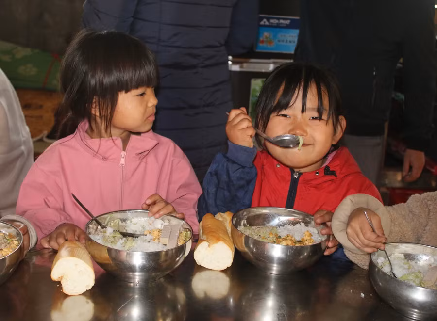 Các em học sinh diện áo mới, vui vẻ ăn bữa cơm trưa cùng đoàn.