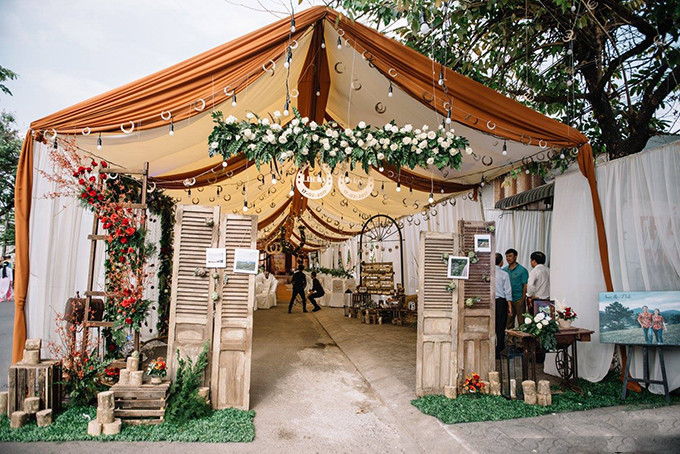 [Caption] Cổng hoa được thiết kế bằng bốn cánh cửa mộc mạc, đính kết hoa artiso. Yếu tố chủ đạo làm nên ý nghĩa cũng như không gian của lễ cưới chính là biểu tượng Horseshoe (Móng ngựa).
