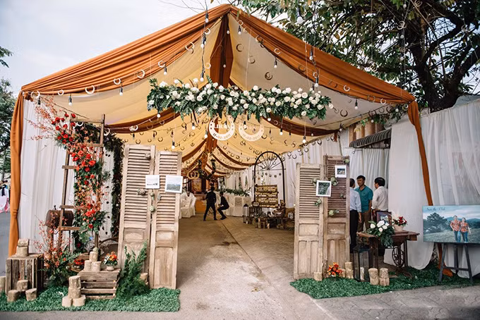 [Caption] Cổng hoa được thiết kế bằng bốn cánh cửa mộc mạc, đính kết hoa artiso. Yếu tố chủ đạo làm nên ý nghĩa cũng như không gian của lễ cưới chính là biểu tượng Horseshoe (Móng ngựa).