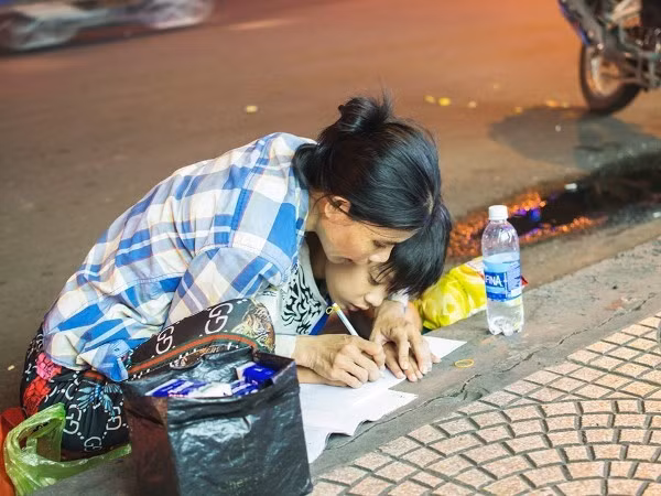 Hình ảnh mẹ cầm tay con dạy từng nét chữ bên lề đường gây xúc động mạnh